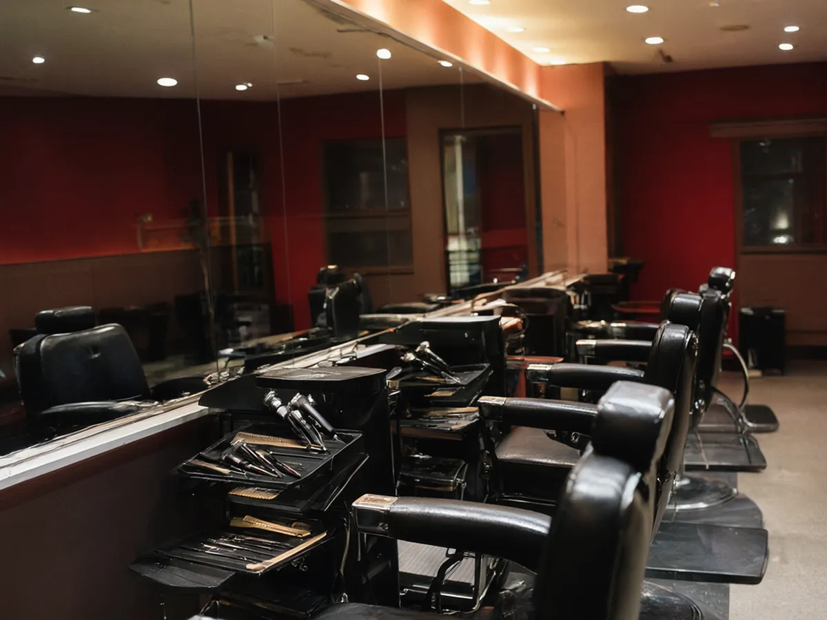 Four black barber chairs facing a long mirror with tool trays at each station