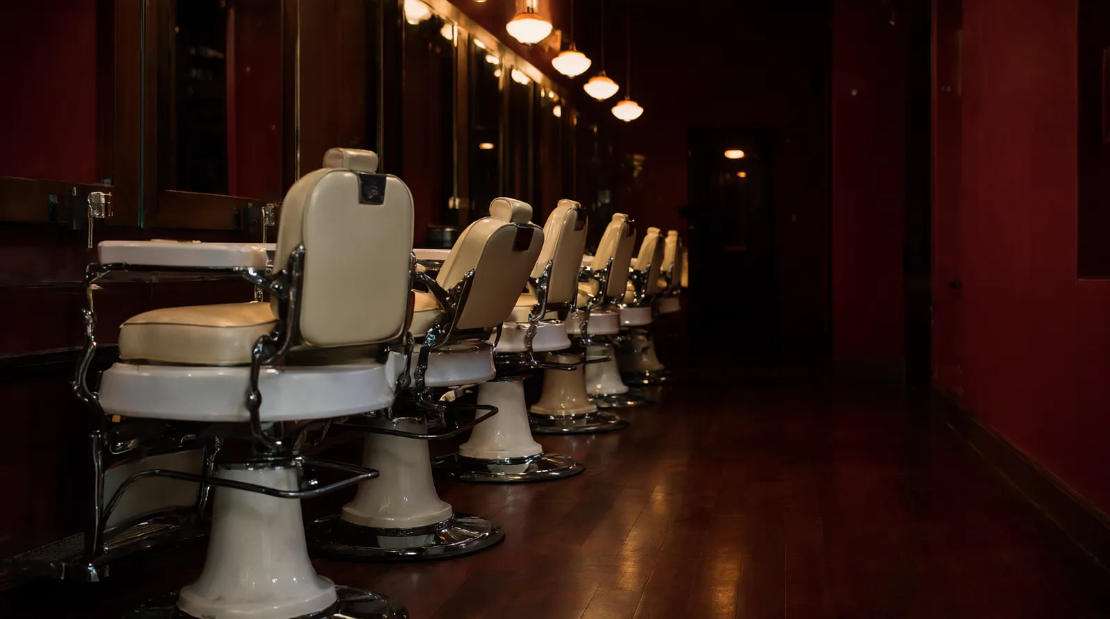 Vintage cream leather barber chairs along a mirrored wall under amber lights